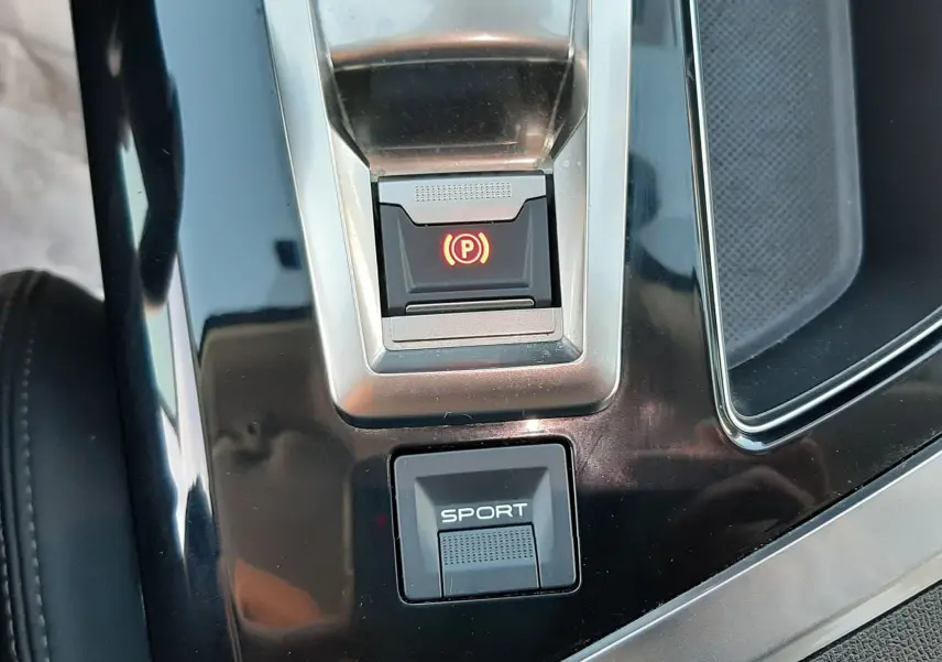 Gros plan sur la console centrale noire du Peugeot 3008 gris Amazonite, avec bouton frein à main électronique et mode Sport.