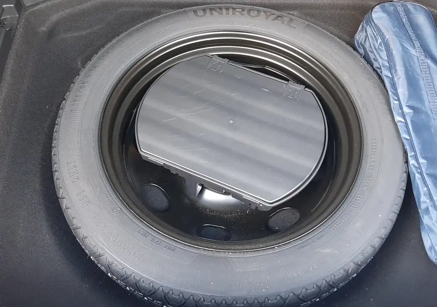 Gros plan sur la roue de secours Uniroyal dans le coffre du Peugeot 3008 gris Amazonite, avec une housse bleue à droite.