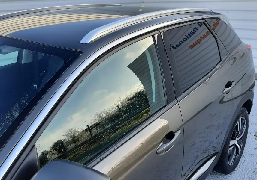 Vue latérale côté gauche du Peugeot 3008 gris amazonite 2019 avec barres de toit et vitres teintées.