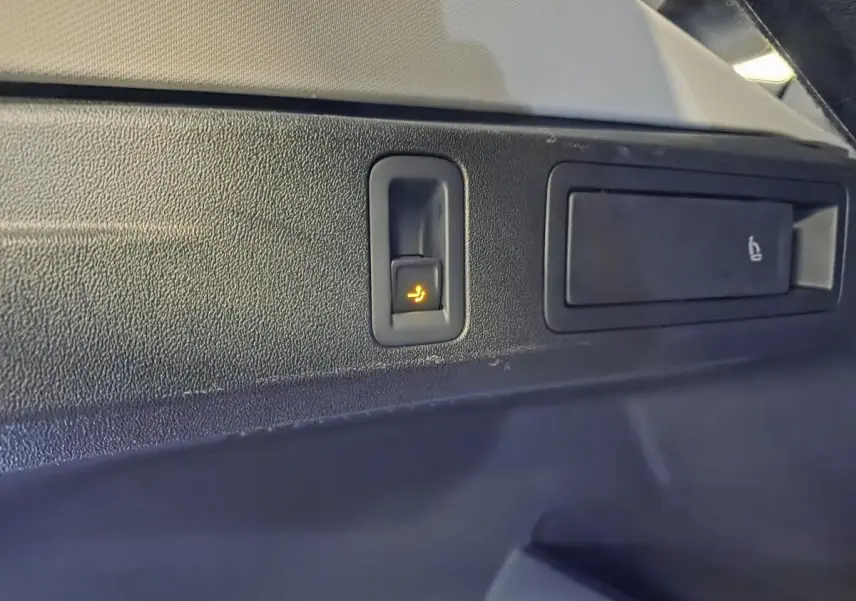 Gros plan sur le bouton de rabattement électrique des sièges arrière dans le coffre du Volkswagen Tiguan noir.