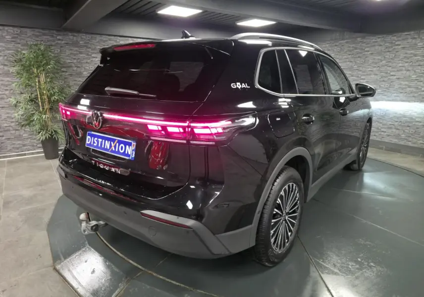Volkswagen Tiguan noir en 3/4 arrière droit avec feux LED allumés et crochet d'attelage escamotable visible.
