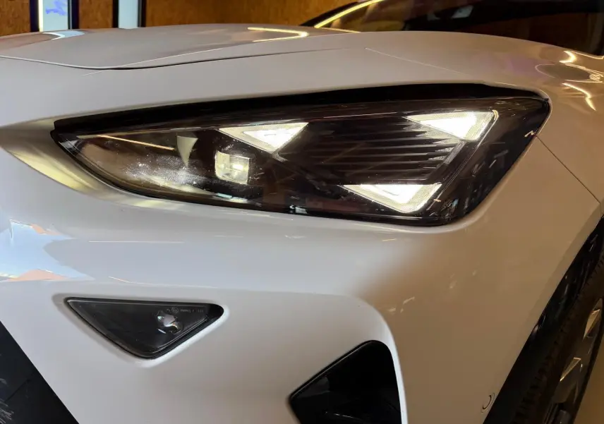 Gros plan sur le phare avant droit blanc du CUPRA Formentor 2.0 TDI 150 DSG7 V avec feux LED triangulaires allumés.