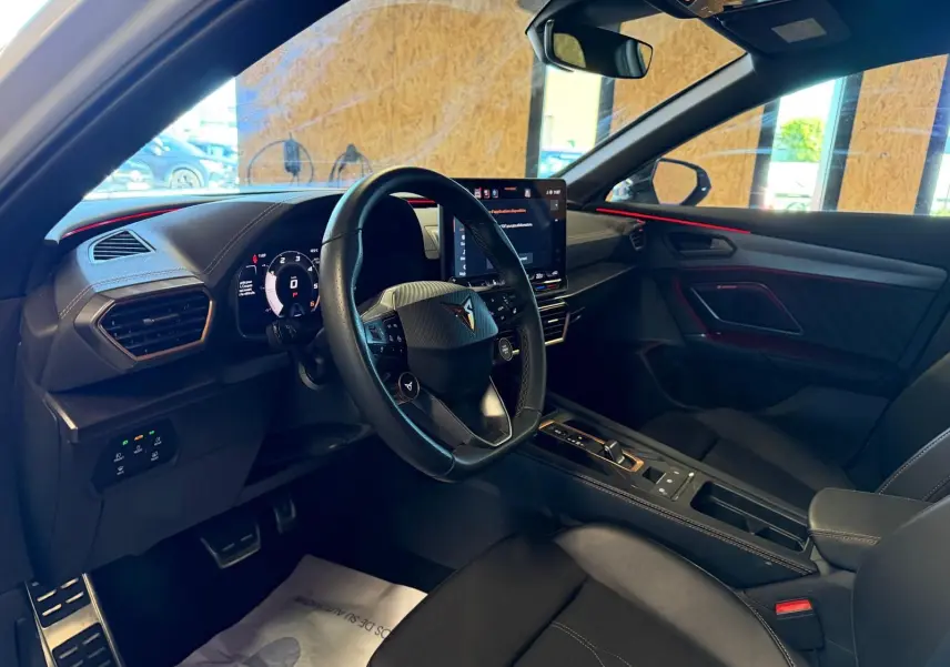 Vue intérieure côté conducteur du CUPRA Formentor 2025, avec volant cuir, écran tactile et éclairage d'ambiance rouge.