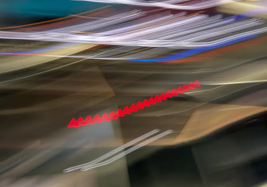 Image floue sans véhicule clairement visible, avec des lumières rouges et blanches étirées sur un fond sombre.