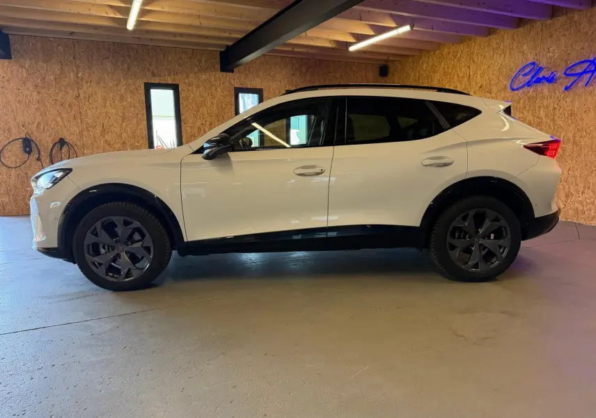 Vue de profil côté gauche d'un CUPRA Formentor blanc 2025 avec jantes noires et vitres arrière surteintées dans un garage.