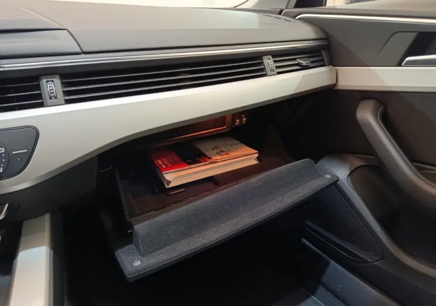 Vue intérieure côté passager de l'Audi A4 35 TFSI 2024, boîte à gants ouverte avec documents visibles.