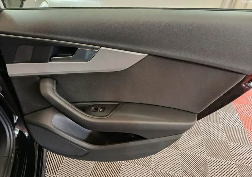 Vue rapprochée de la porte avant gauche noire de l'Audi A4 35 TFSI 2024 avec poignée et commande de vitre.