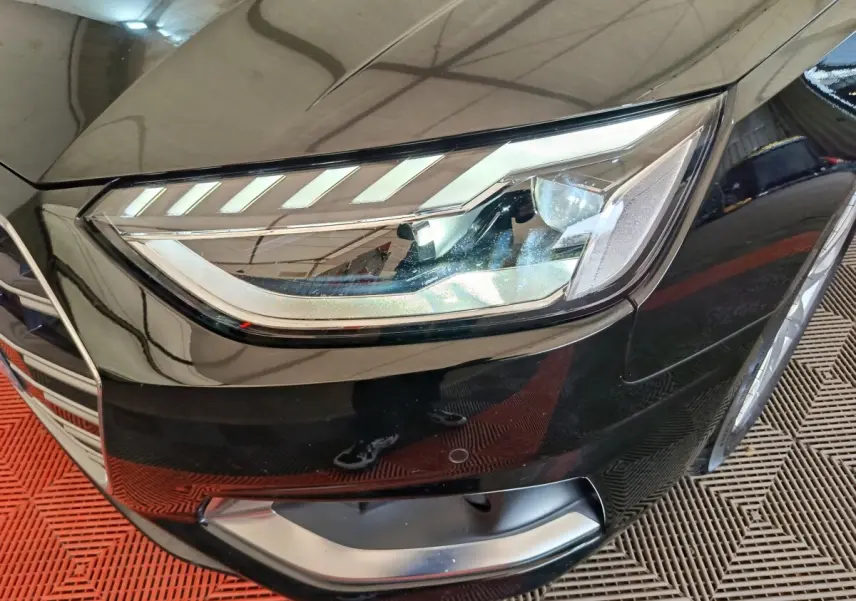 Gros plan sur le phare avant droit d'une Audi A4 35 TFSI noire, avec calandre et partie du pare-chocs visibles.