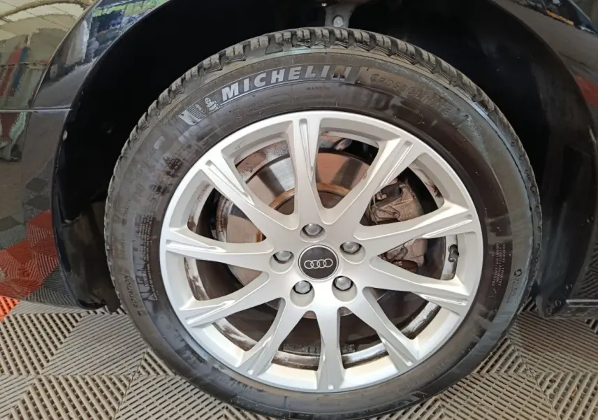 Gros plan sur la roue avant droite d'une Audi A4 noire 2024 avec jante argentée et pneu Michelin CrossClimate.
