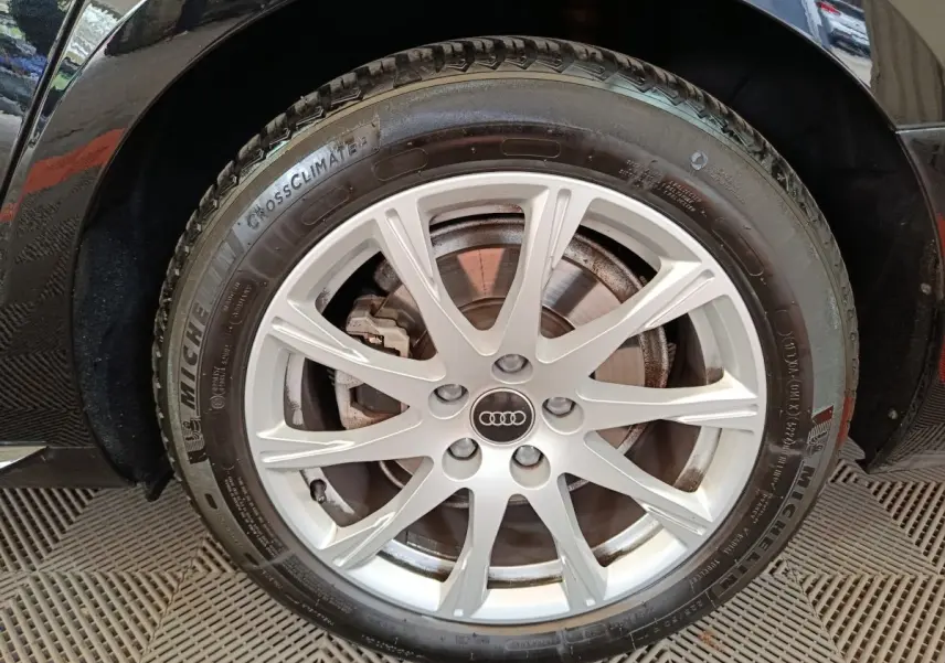 Gros plan sur la roue avant droite d'une Audi A4 noire, jante alliage argentée avec logo Audi central.