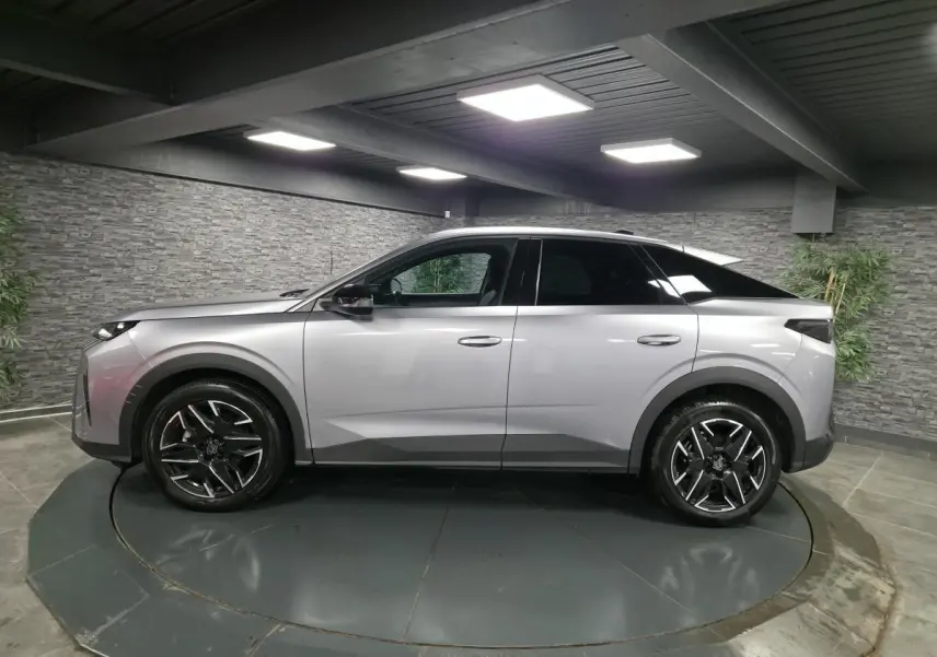 Vue de profil côté gauche d’un Peugeot 3008 gris métallisé avec jantes alliage noires et toit noir dans un showroom.