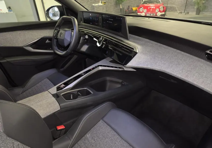 Intérieur de la Peugeot 3008 Hybrid 2025 vu côté passager, avec tableau de bord et console centrale en tissu gris chiné.