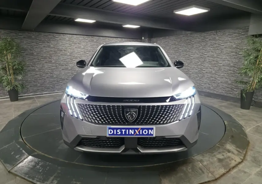 Vue avant frontale d'un Peugeot 3008 gris métallisé avec calandre noire laquée et feux LED allumés dans un showroom.