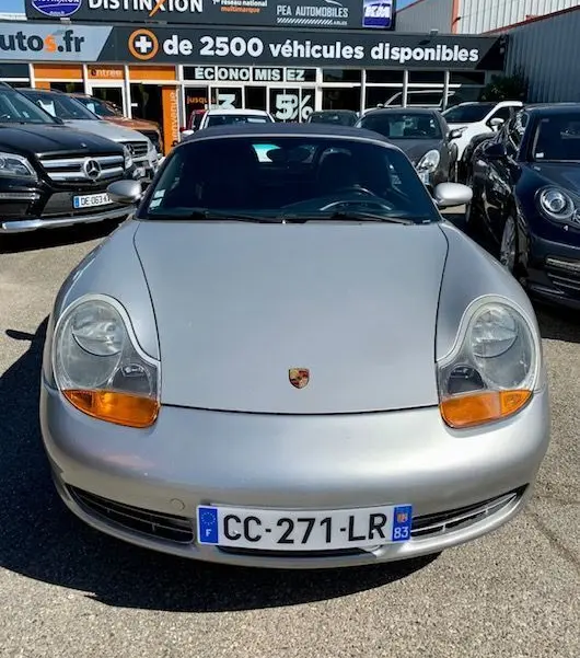 Vue frontale d'une Porsche Boxster 986 gris clair de 2001, avec phares ovales et plaque d'immatriculation française visible.