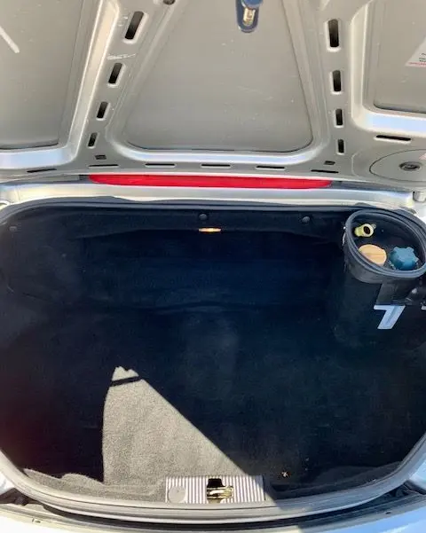 Coffre ouvert vu de dessus du Porsche Boxster 986 gris 2001, montrant l'intérieur noir et un compartiment latéral.