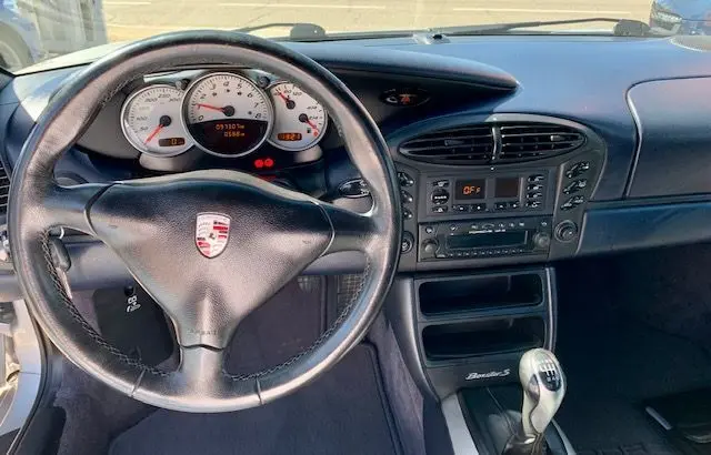 Intérieur avant du Porsche Boxster 986 3.2 S gris de 2001, volant cuir, tableau de bord blanc et levier de vitesse manuel.