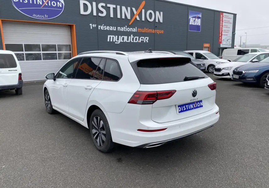 Volkswagen Golf SW blanc oryx vue 3/4 arrière droit avec vitres arrière surteintées sur parking de concession.