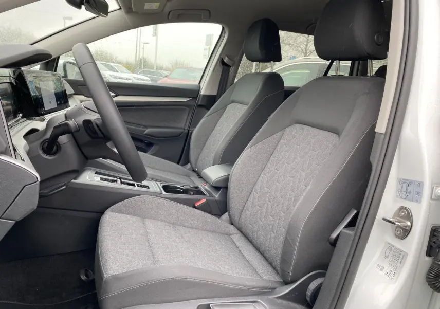 Vue intérieure côté conducteur de la Volkswagen Golf SW 2.0 TDI 116 DSG 7 Active Move avec sièges tissu gris et portière blanche ouverte.