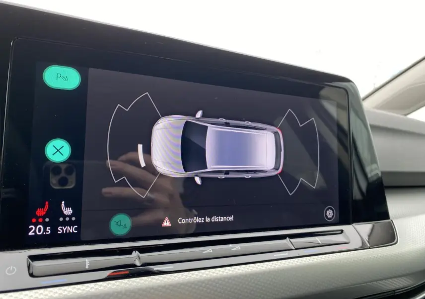 Écran tactile intérieur de la Volkswagen Golf SW 2.0 TDI montrant l'aide au stationnement avec vue aérienne du véhicule blanc oryx.