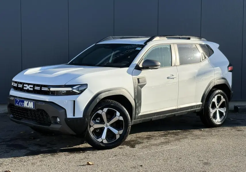 SUV Dacia Duster blanc glacier en 3/4 avant droit, avec jantes alliage et barres de toit noires visibles.
