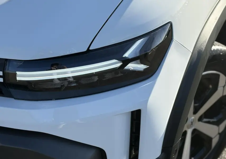 Gros plan sur le phare avant droit blanc glacier du Dacia Duster 2026 avec jante alliage visible en arrière-plan.
