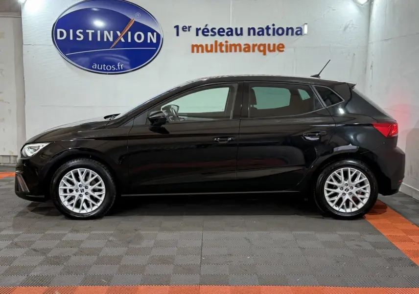 Profil latéral droit d'une SEAT IBIZA 1.0 TSI 110 FR noire, avec jantes alliage et rétroviseurs ton caisse dans un showroom.