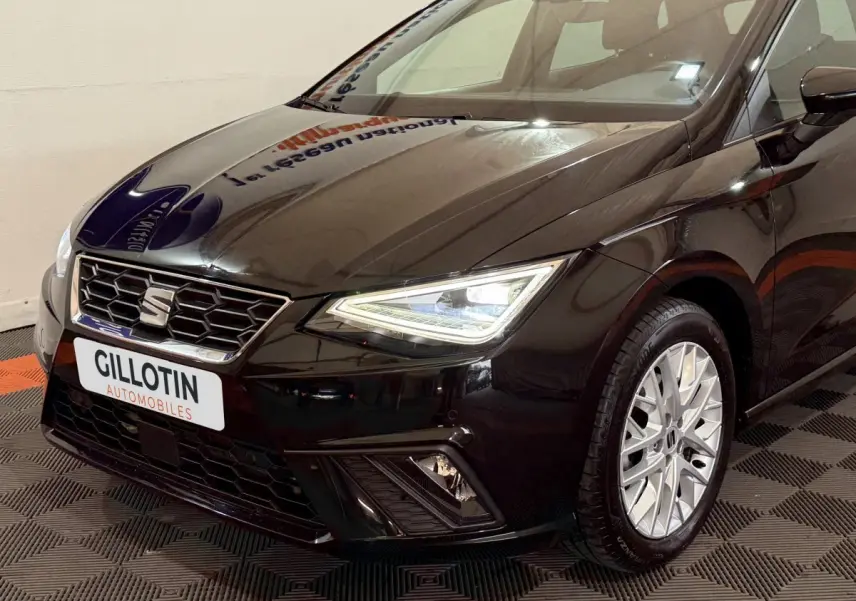 Vue 3/4 avant droit d'une SEAT Ibiza noire 2024 avec phares LED allumés et jantes argentées détaillées.