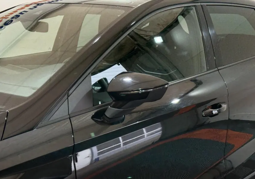 Vue rapprochée du côté gauche avant d'une SEAT Ibiza noire 2024, mettant en valeur le rétroviseur caméra et la poignée de porte.