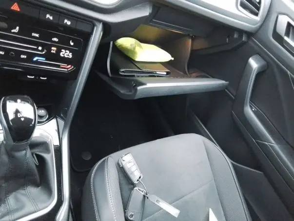 Vue intérieure côté passager du Volkswagen T-Roc 2025 blanc toit noir, avec boîte auto et boîte à gants ouverte contenant un objet jaune.