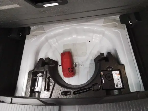 Coffre ouvert d’un Volkswagen T-Roc blanc toit noir, vue plongeante sur le rangement d’outils et kit de secours.