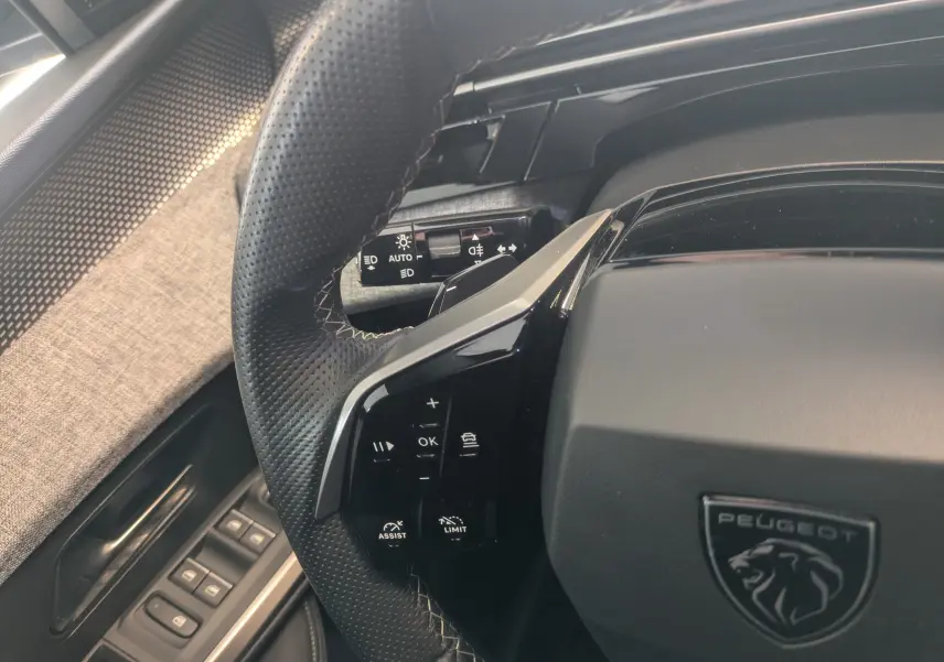 Gros plan sur le volant perforé noir du Peugeot 5008 hybride 2025 avec commandes intégrées et logo lion central.