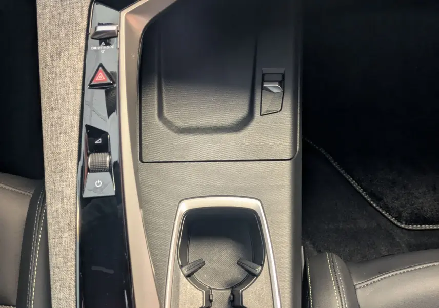 Vue plongeante sur la console centrale noire et grise du Peugeot 5008 hybride 2025 avec porte-gobelets et commandes tactiles.