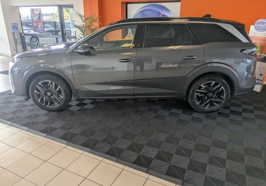 Peugeot 5008 hybride gris titane avec toit noir, vue profil côté gauche en intérieur showroom.