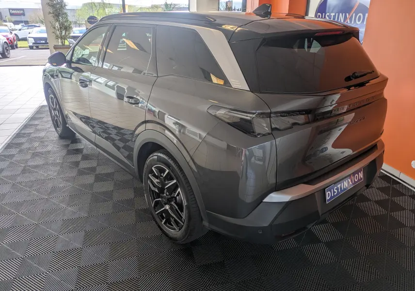 Vue 3/4 arrière droite d’un Peugeot 5008 gris titane avec toit noir et jantes alliage noires en showroom.