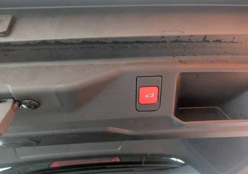 Bouton rouge d'ouverture électrique du hayon visible sur l'intérieur du coffre d'un Peugeot 5008 hybride gris titane.