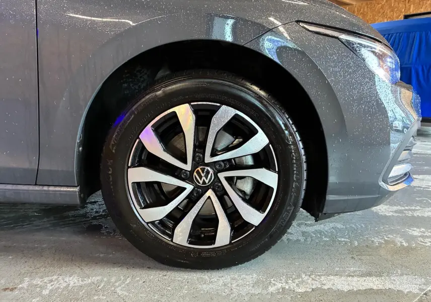 Gros plan sur la roue avant gauche d'une Volkswagen Golf gris 2022 avec jante alliage bicolore et carrosserie mouillée.