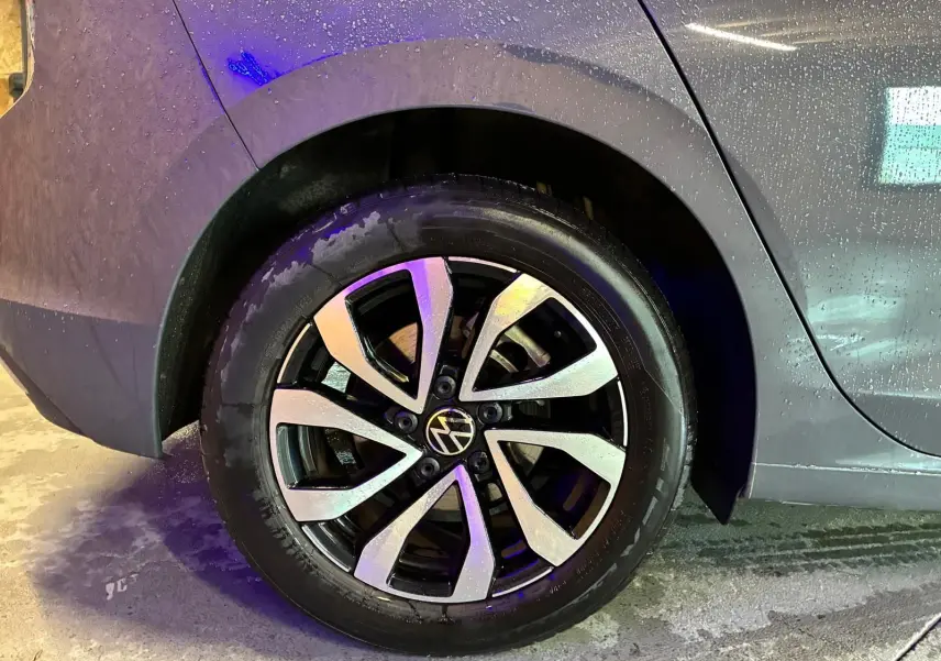 Gros plan sur la roue arrière droite d’une Volkswagen Golf gris 2022, avec jante alliage bicolore et carrosserie mouillée.