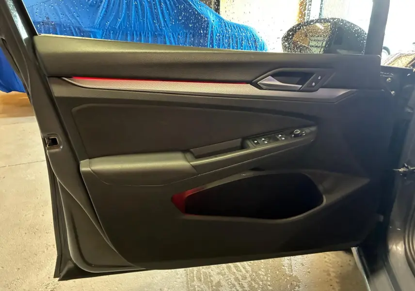 Vue intérieure côté gauche de la porte avant d’une Volkswagen Golf gris 1.5 eTSI 130 DSG7 avec éclairage d’ambiance rouge.