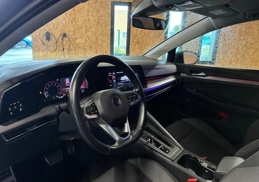 Vue intérieure côté conducteur de la Volkswagen Golf 1.5 eTSI 130 DSG7 Active 2022 avec tableau de bord numérique et ambiance lumineuse rouge.