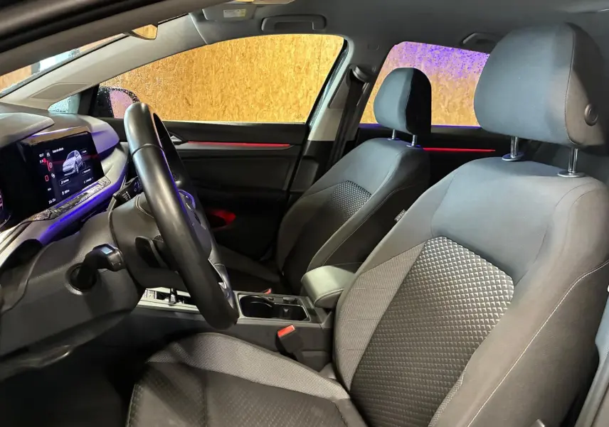 Intérieur avant de la Volkswagen Golf 1.5 eTSI 130 DSG7 Active 2022, vue côté conducteur, sièges tissu noir et éclairage d’ambiance rouge.