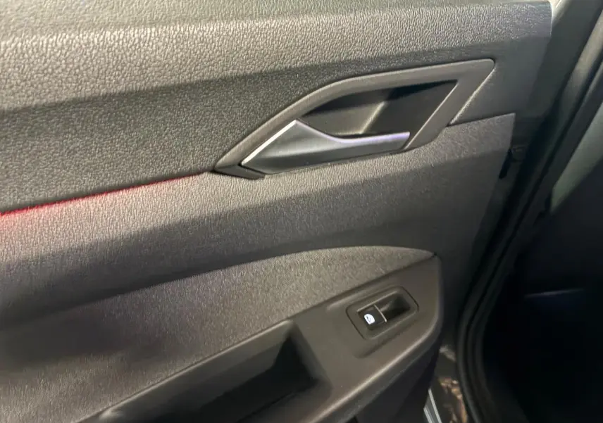 Détail de la porte intérieure côté droit de la Volkswagen Golf gris, avec poignée argentée et bouton de lève-vitre.