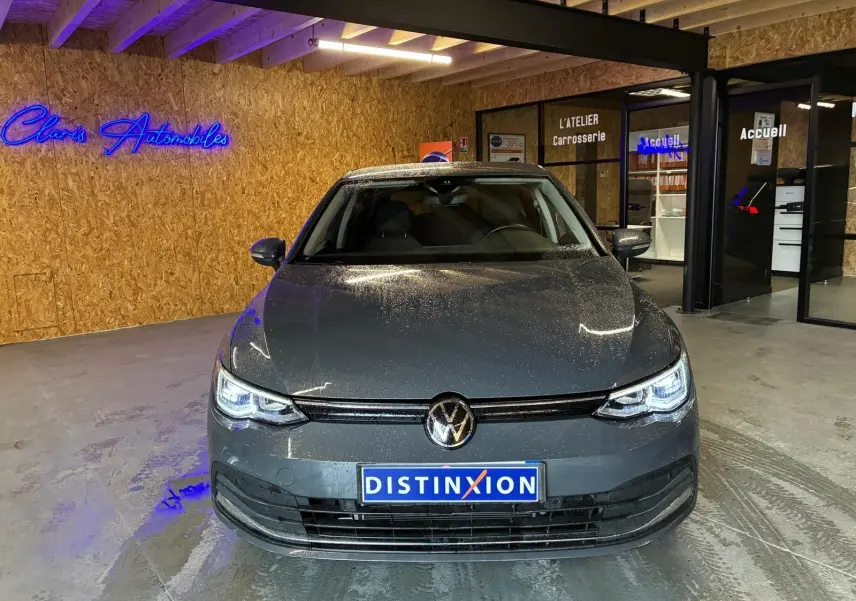 Vue de face d'une Volkswagen Golf 1.5 eTSI gris métallisé 2022, avec phares LED allumés dans un showroom intérieur.