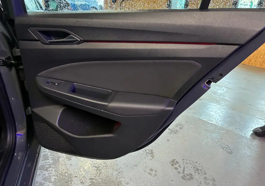 Vue intérieure de la porte arrière droite d'une Volkswagen Golf gris 2022 avec garniture noire et éclairage d'ambiance rouge.