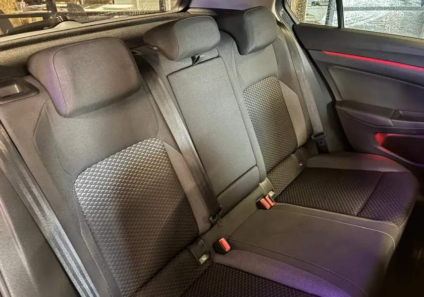 Vue intérieure sur la banquette arrière en tissu noir avec motifs géométriques et éclairage d'ambiance rouge côté droit.