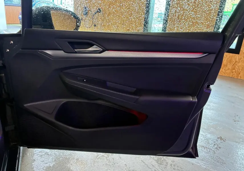 Vue intérieure de la porte avant gauche de la Volkswagen Golf gris, avec éclairage d'ambiance rouge et insert décoratif.