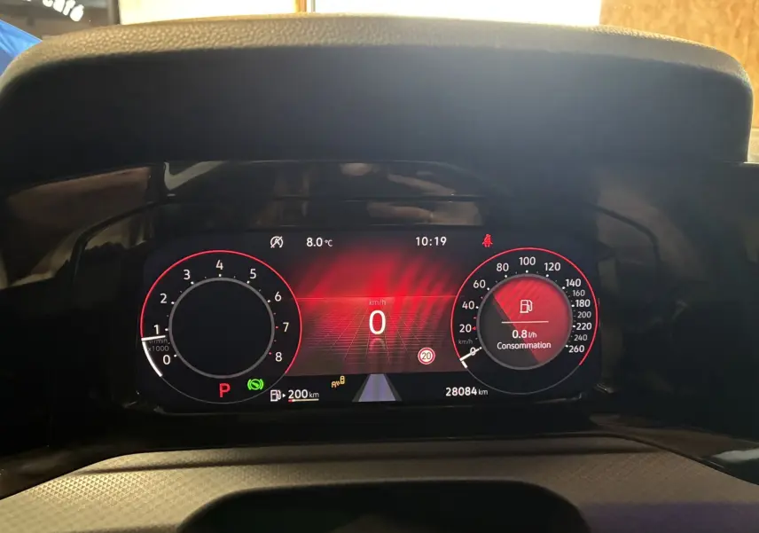 Vue rapprochée du tableau de bord numérique de la Volkswagen Golf gris, affichant la consommation et la vitesse à l'arrêt.