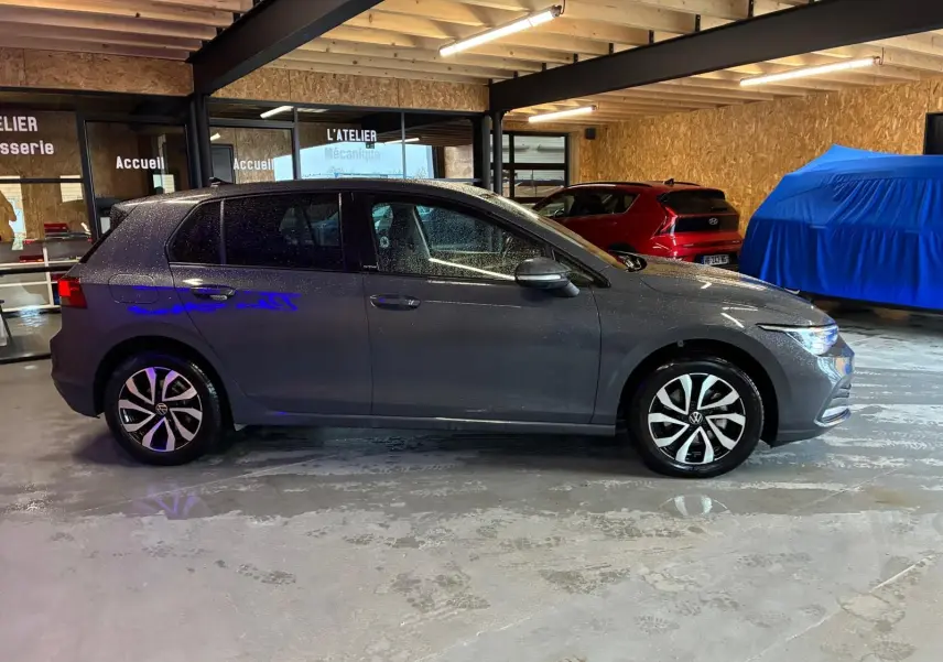 Vue de profil côté gauche d'une Volkswagen Golf gris métallisé 2022 stationnée en intérieur avec jantes distinctives.