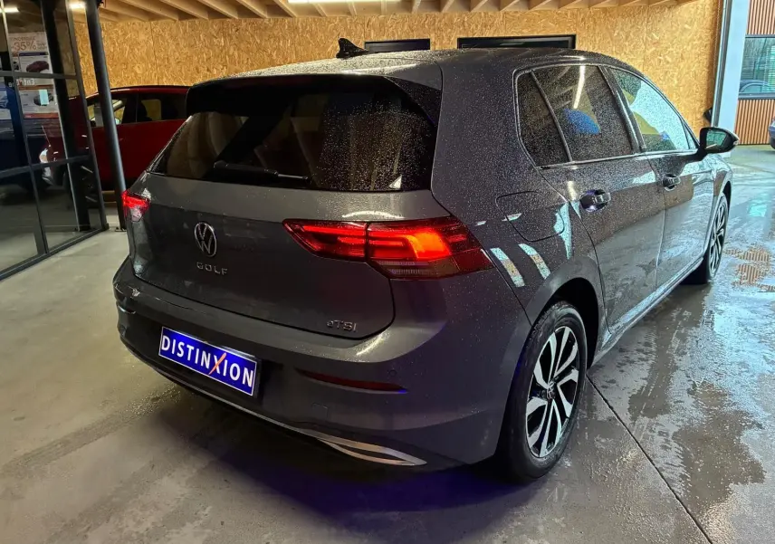 Vue 3/4 arrière droite d'une Volkswagen Golf gris métallisé 5 portes avec feux arrière allumés en intérieur showroom.