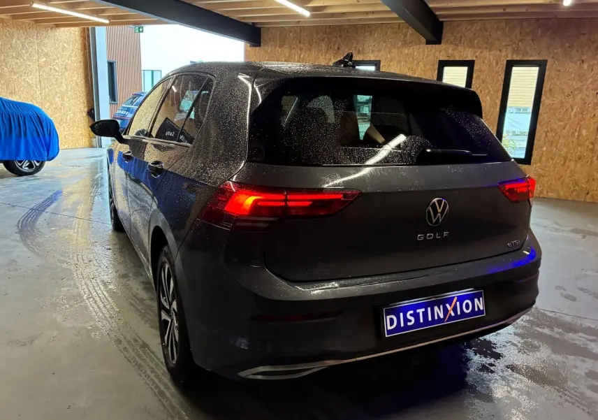 Vue 3/4 arrière droite d'une Volkswagen Golf gris foncé 1.5 eTSI 130 DSG7 Active avec feux arrière allumés en intérieur.