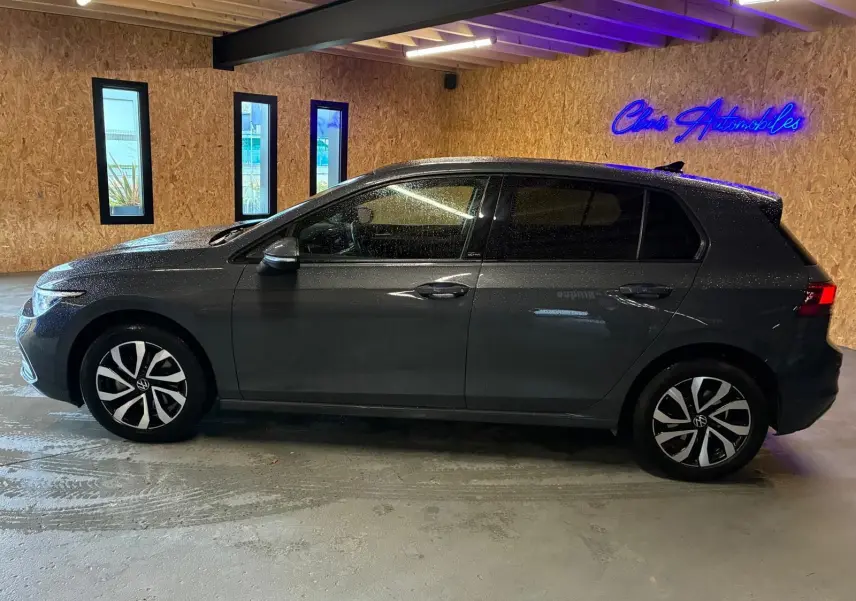 Vue de profil côté gauche d'une Volkswagen Golf gris métallisé 5 portes, stationnée en intérieur avec éclairage néon bleu.